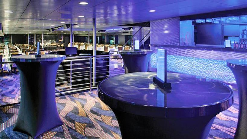 Modern yacht lounge with cocktail tables and illuminated bar area.